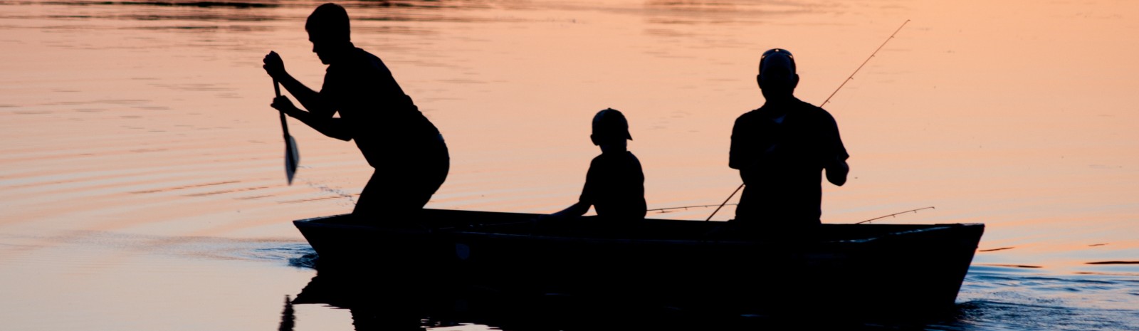 Young boy fishing at dusk with family.